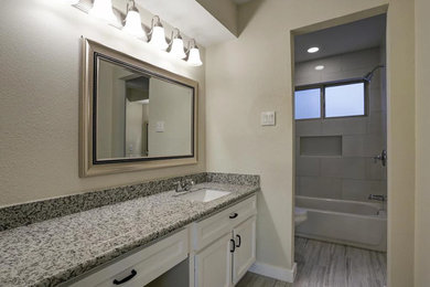 This is an example of a medium sized traditional shower room bathroom in Orange County with shaker cabinets, white cabinets, a shower/bath combination, a two-piece toilet, grey tiles, porcelain tiles, beige walls, vinyl flooring, a submerged sink, granite worktops, an alcove bath, grey floors and a shower curtain.
