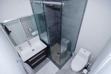 Small minimalist 3/4 gray tile and porcelain tile porcelain tile and gray floor corner shower photo in Austin with flat-panel cabinets, black cabinets, a one-piece toilet, white walls, a drop-in sink and a hinged shower door