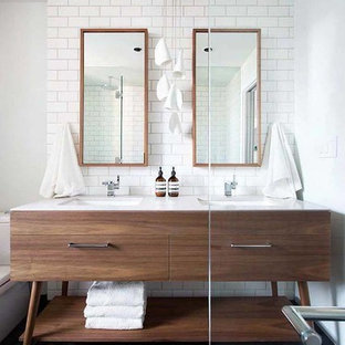 Foto på ett stort 50 tals en-suite badrum, med vit kakel, vita väggar, klinkergolv i keramik, ett undermonterad handfat, bänkskiva i akrylsten, släta luckor, skåp i mörkt trä, en toalettstol med separat cisternkåpa, tunnelbanekakel och grått golv