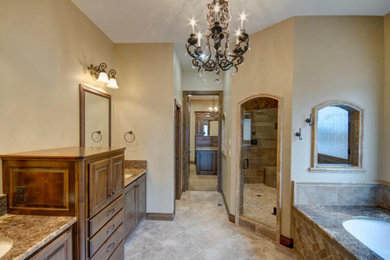 Cette image montre une salle de bain principale chalet en bois brun de taille moyenne avec un placard avec porte à panneau surélevé, une baignoire encastrée, une douche double, un carrelage beige, un carrelage de pierre, un mur beige, un sol en travertin, un lavabo encastré et un plan de toilette en granite.