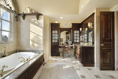 Immagine di una grande stanza da bagno padronale chic con ante con bugna sagomata, ante in legno bruno, vasca ad alcova, doccia alcova, pareti beige, pavimento in marmo e top in granito
