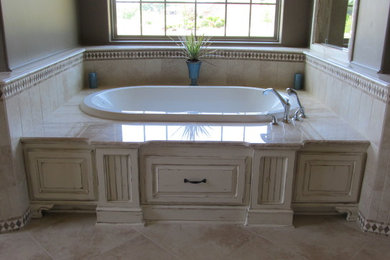Example of a large cottage chic master beige tile and stone tile limestone floor drop-in bathtub design in San Diego with beige walls, raised-panel cabinets, distressed cabinets and limestone countertops