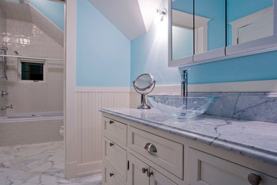 ミネアポリスにある小さなトランジショナルスタイルのおしゃれな子供用バスルーム (落し込みパネル扉のキャビネット、白いキャビネット、ドロップイン型浴槽、シャワー付き浴槽	、一体型トイレ	、白いタイル、磁器タイル、青い壁、大理石の床、ベッセル式洗面器、大理石の洗面台、白い床) の写真