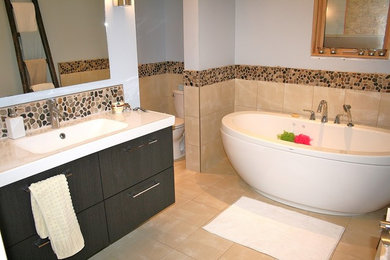 This is an example of a large contemporary ensuite bathroom in Vancouver with flat-panel cabinets, black cabinets, a freestanding bath, a two-piece toilet, beige tiles, pebble tiles, blue walls, ceramic flooring, an integrated sink and engineered stone worktops.