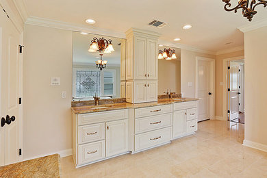 Large traditional ensuite bathroom in New Orleans with raised-panel cabinets, white cabinets, beige walls, a submerged sink, granite worktops, beige floors, a built-in bath and limestone flooring.