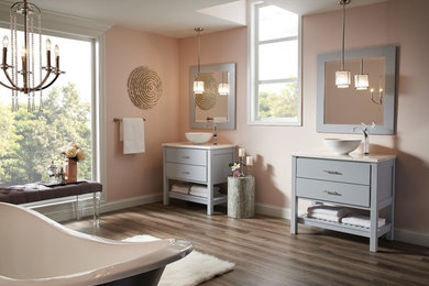 Modern inredning av ett stort en-suite badrum, med möbel-liknande, grå skåp, ett badkar med tassar, rosa väggar, mörkt trägolv, ett fristående handfat och bänkskiva i akrylsten