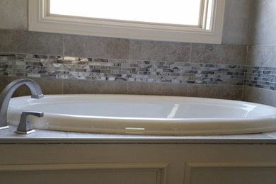 オクラホマシティにあるコンテンポラリースタイルのおしゃれな浴室 (ドロップイン型浴槽、ベージュのタイル、セラミックタイル、グレーの壁) の写真