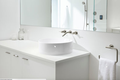 Пример оригинального дизайна: ванная комната среднего размера в стиле модернизм с плоскими фасадами, белыми фасадами, белой плиткой, белыми стенами, душевой кабиной, настольной раковиной и столешницей из искусственного кварца