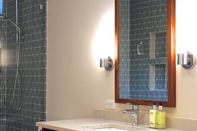 ダラスにある中くらいなミッドセンチュリースタイルのおしゃれなマスターバスルーム (フラットパネル扉のキャビネット、中間色木目調キャビネット、オープン型シャワー、一体型トイレ	、青いタイル、ガラス板タイル、白い壁、磁器タイルの床、アンダーカウンター洗面器、クオーツストーンの洗面台) の写真
