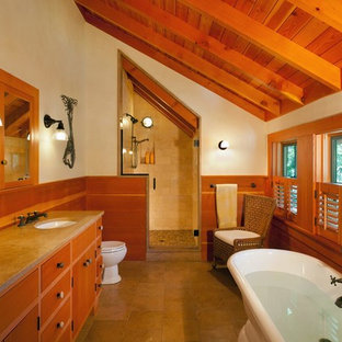 This is an example of a mid-sized country master bathroom in Boston with flat-panel cabinets, medium wood cabinets, a claw-foot tub, an alcove shower, a two-piece toilet, beige tile, stone tile, beige walls, travertine floors, an undermount sink and engineered quartz benchtops.