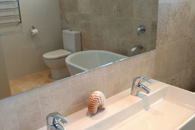 Пример оригинального дизайна: большая главная ванная комната в стиле модернизм с отдельно стоящей ванной, фасадами цвета дерева среднего тона, плиткой из травертина, мраморным полом и раковиной с несколькими смесителями