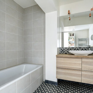 Inspiration pour une salle d'eau nordique avec un placard à porte plane, des portes de placard en bois brun, une baignoire posée, un carrelage gris, un mur blanc, une vasque, un plan de toilette en bois, un sol multicolore et un plan de toilette marron.