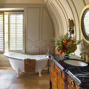 Idee per una stanza da bagno padronale vittoriana con consolle stile comò, ante in legno scuro, vasca con piedi a zampa di leone, pareti beige, lavabo sottopiano, top in marmo, pavimento beige e top nero