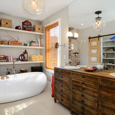 Eclectic beige tile freestanding bathtub photo in New York with a drop-in sink, furniture-like cabinets, dark wood cabinets, wood countertops, beige walls and brown countertops