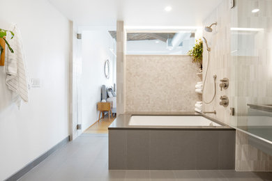 Medium sized contemporary ensuite bathroom in Portland with flat-panel cabinets, medium wood cabinets, a submerged bath, a shower/bath combination, grey tiles, marble tiles, white walls, porcelain flooring, engineered stone worktops, grey floors, a hinged door and grey worktops.