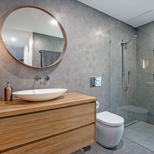 Design ideas for a mid-sized contemporary 3/4 bathroom in Sunshine Coast with medium wood cabinets, gray tile, porcelain tile, grey walls, porcelain floors, a vessel sink, wood benchtops, grey floor, an open shower, flat-panel cabinets, a curbless shower, a one-piece toilet and brown benchtops.