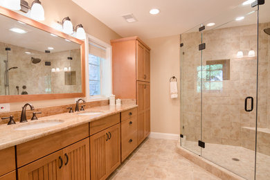Photo of a large traditional ensuite bathroom in DC Metro with beaded cabinets, medium wood cabinets, granite worktops, beige tiles, porcelain tiles, a double shower, a two-piece toilet, a submerged sink, beige walls and porcelain flooring.