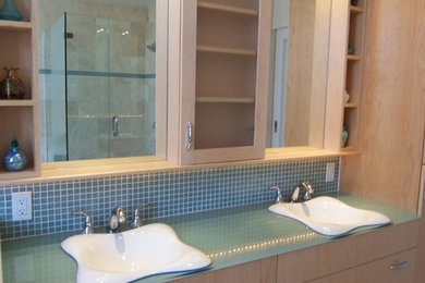 Photo of a medium sized contemporary ensuite bathroom in Philadelphia with a built-in sink, flat-panel cabinets, light wood cabinets, glass worktops, a built-in bath, a double shower, blue tiles, glass tiles, beige walls and travertine flooring.