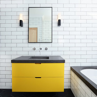 Contemporary master bathroom in Melbourne with flat-panel cabinets, yellow cabinets, a corner tub, a curbless shower, white tile, subway tile, white walls, an undermount sink, concrete benchtops, black floor and grey benchtops.