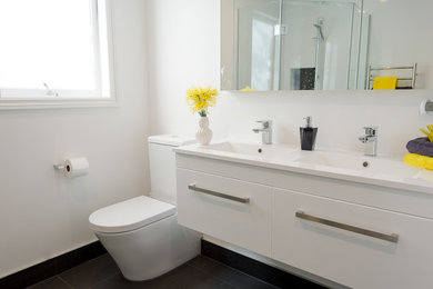 オークランドにあるお手頃価格の中くらいなコンテンポラリースタイルのおしゃれなマスターバスルーム (オーバーカウンターシンク、フラットパネル扉のキャビネット、白いキャビネット、置き型浴槽、コーナー設置型シャワー、一体型トイレ	、黒いタイル、セラミックタイル、白い壁、セラミックタイルの床) の写真
