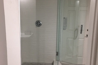 Example of a trendy white tile gray floor corner shower design in Tampa with a hinged shower door