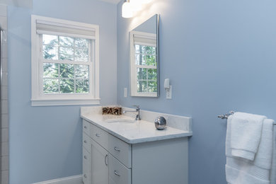 Example of a mid-sized transitional 3/4 subway tile and blue tile white floor and ceramic tile corner shower design in Raleigh with white cabinets, a one-piece toilet, blue walls, an undermount sink, a hinged shower door, quartz countertops, shaker cabinets and white countertops