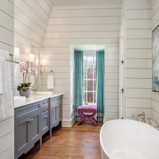 Example of a transitional dark wood floor, brown floor, double-sink and shiplap wall freestanding bathtub design in Other with shaker cabinets, gray cabinets, white walls, a vessel sink, white countertops and a built-in vanity