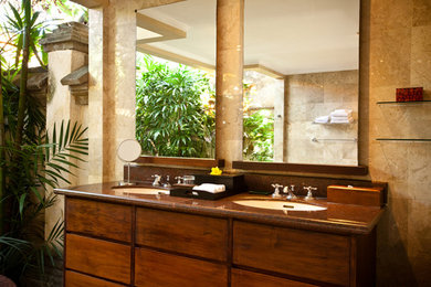 Aménagement d'une salle de bain principale en bois brun avec un placard à porte plane, un plan de toilette en verre, une baignoire posée, un carrelage marron et un carrelage en pâte de verre.