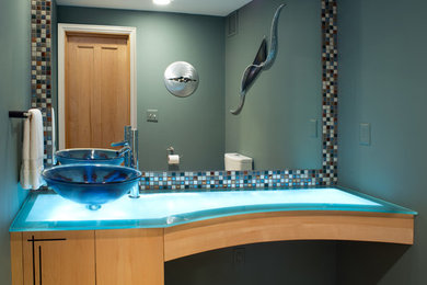 This is an example of a contemporary bathroom in Columbus with a vessel sink, flat-panel cabinets, light wood cabinets, glass worktops, a two-piece toilet, multi-coloured tiles, mosaic tiles, green walls and slate flooring.