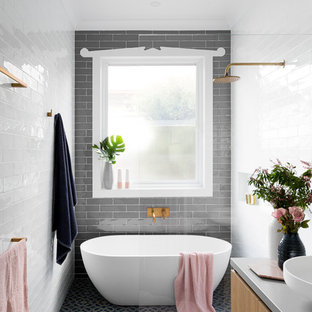 Foto på ett stort funkis grå en-suite badrum, med släta luckor, skåp i mellenmörkt trä, ett fristående badkar, en öppen dusch, grå kakel, vit kakel, tunnelbanekakel, ett fristående handfat, med dusch som är öppen, en toalettstol med separat cisternkåpa, grå väggar, klinkergolv i keramik, bänkskiva i betong och blått golv