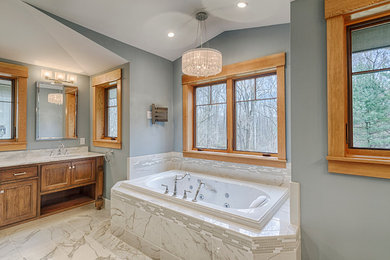Example of a large classic master marble floor and gray floor drop-in bathtub design in Baltimore with raised-panel cabinets, brown cabinets, gray walls, an undermount sink and granite countertops