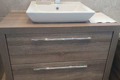 This is an example of a medium sized modern bathroom in Surrey with flat-panel cabinets, medium wood cabinets, grey tiles, ceramic tiles, grey walls, vinyl flooring, a vessel sink, laminate worktops, multi-coloured floors and brown worktops.