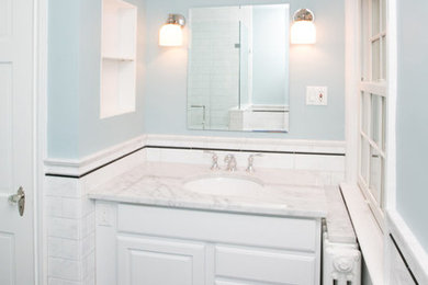 ワシントンD.C.にある中くらいなトランジショナルスタイルのおしゃれなバスルーム (浴槽なし) (レイズドパネル扉のキャビネット、白いキャビネット、白いタイル、青い壁、アンダーカウンター洗面器、大理石の洗面台、黒い床) の写真
