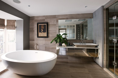 ロンドンにあるコンテンポラリースタイルのおしゃれな浴室 (ベッセル式洗面器、置き型浴槽、ベージュのタイル、グレーの壁) の写真