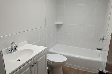他の地域にある中くらいなトランジショナルスタイルのおしゃれなバスルーム (浴槽なし) (レイズドパネル扉のキャビネット、白いキャビネット、アルコーブ型浴槽、シャワー付き浴槽	、壁掛け式トイレ、白いタイル、磁器タイル、白い壁、濃色無垢フローリング、一体型シンク、人工大理石カウンター、茶色い床、シャワーカーテン、白い洗面カウンター) の写真