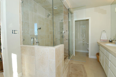 Alcove shower - mid-sized traditional master beige tile and stone tile travertine floor and brown floor alcove shower idea in San Francisco with flat-panel cabinets, white cabinets, beige walls, a drop-in sink and a hinged shower door