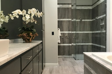 This is an example of a large modern ensuite bathroom in Dallas with flat-panel cabinets, grey cabinets, a built-in bath, a double shower, a two-piece toilet, grey tiles, porcelain tiles, grey walls, porcelain flooring, a vessel sink, marble worktops, grey floors and grey worktops.