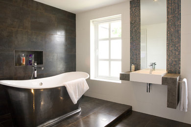 Inspiration för stora moderna grått en-suite badrum, med ett fristående badkar, en vägghängd toalettstol, brun kakel, porslinskakel, bruna väggar, klinkergolv i porslin, ett väggmonterat handfat, öppna hyllor, grå skåp, en öppen dusch, granitbänkskiva, brunt golv och med dusch som är öppen