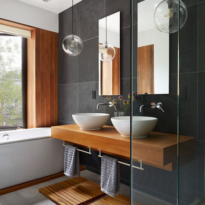 Example of a trendy black tile and slate tile drop-in bathtub design in New York with a vessel sink, wood countertops and brown countertops