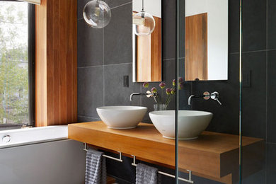 Ejemplo de cuarto de baño principal actual con bañera encastrada, ducha esquinera, baldosas y/o azulejos negros, paredes negras, lavabo sobreencimera, encimera de madera y suelo gris