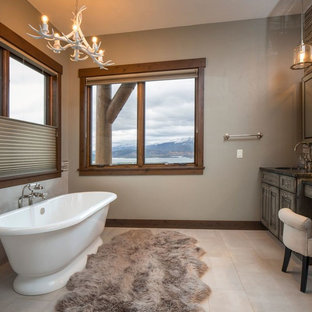Ispirazione per una stanza da bagno padronale rustica di medie dimensioni con vasca freestanding, lavabo sottopiano, ante con bugna sagomata, ante con finitura invecchiata, piastrelle beige, piastrelle marroni, piastrelle di vetro, pareti beige, pavimento in gres porcellanato, top in quarzite, pavimento beige e top nero