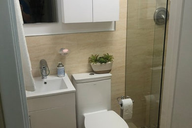 Пример оригинального дизайна: ванная комната среднего размера в стиле модернизм с плоскими фасадами, белыми фасадами, душевой кабиной, душем в нише, унитазом-моноблоком, бежевой плиткой, каменной плиткой, белыми стенами, полом из керамогранита, врезной раковиной, столешницей из искусственного камня, коричневым полом, душем с раздвижными дверями и белой столешницей