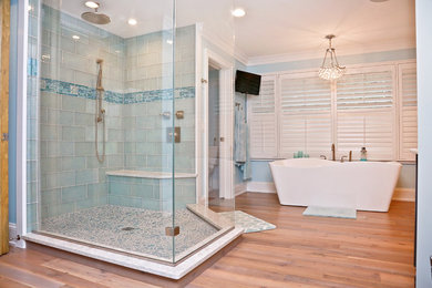 Imagen de cuarto de baño principal costero con puertas de armario de madera en tonos medios, bañera exenta, ducha abierta, baldosas y/o azulejos azules, suelo de madera clara, encimera de cuarcita y ducha abierta