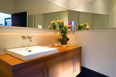 Modelo de cuarto de baño moderno de tamaño medio con armarios con paneles lisos, puertas de armario de madera oscura, paredes beige, lavabo encastrado y encimera de madera
