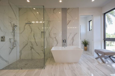 Example of a trendy master white tile marble floor and white floor bathroom design in Miami with flat-panel cabinets, medium tone wood cabinets, white walls, solid surface countertops and a hinged shower door