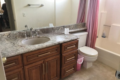 Mid-sized elegant 3/4 beige floor bathroom photo in San Diego with raised-panel cabinets, medium tone wood cabinets, a two-piece toilet, an undermount sink and granite countertops
