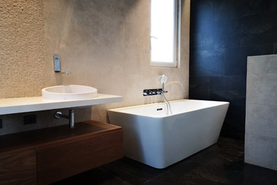 Photo of a medium sized contemporary ensuite bathroom with flat-panel cabinets, dark wood cabinets, a freestanding bath, beige tiles, beige walls, ceramic flooring, a built-in sink, black floors, white worktops, a walk-in shower, an open shower and a one-piece toilet.