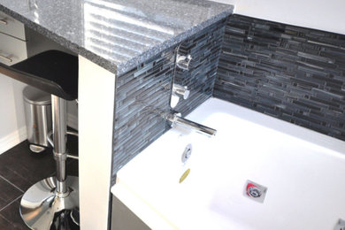 Modelo de cuarto de baño moderno de tamaño medio con armarios con paneles lisos, puertas de armario grises, sanitario de pared, paredes grises, suelo de pizarra, aseo y ducha, encimera de granito y suelo negro