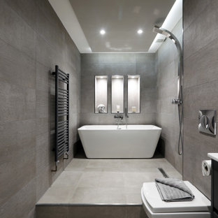 This is an example of a large contemporary bathroom in Sussex with flat-panel cabinets, black cabinets, a freestanding bath, a wall mounted toilet, grey tiles, an integrated sink, grey floors, an open shower, white worktops and a wall niche.