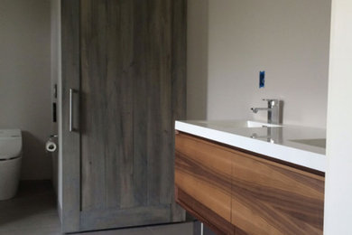 Example of a mid-sized trendy 3/4 ceramic tile and gray floor bathroom design in San Diego with flat-panel cabinets, brown cabinets, a one-piece toilet, beige walls, an integrated sink and quartz countertops